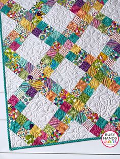 a quilted table topper with colorful squares and flowers on the edges, sitting on a white wooden surface