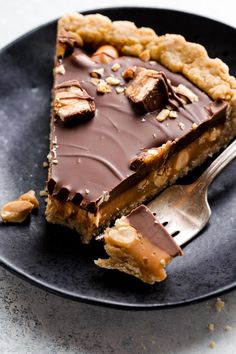 a piece of chocolate pie on a black plate with a fork in front of it