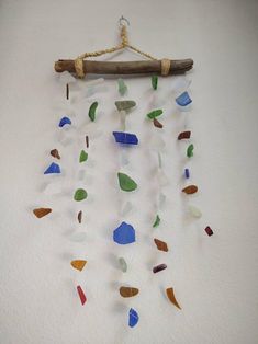 a wind chime made out of sea glass and driftwood on a white wall