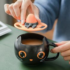 a person holding a black mug with an orange cat design on the inside and bottom