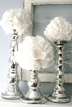 three silver candlesticks with white flowers in them sitting on a shelf next to a mirror