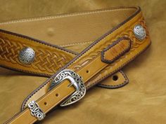 a tan leather belt with silver buckles and braiding on the bottom, sitting on a brown background