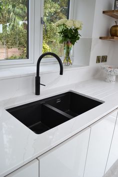 a kitchen sink with two black faucets and a window in the back ground