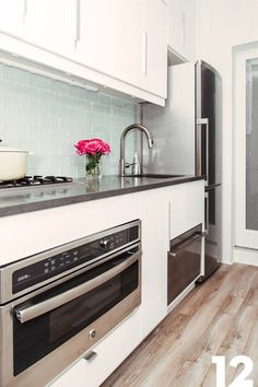 a white kitchen with stainless steel appliances and wood flooring is featured in this image