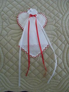 an angel ornament with red ribbon on top of a quilted bed spread