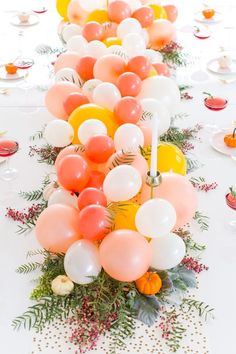 a long table topped with lots of balloons and greenery on top of white plates