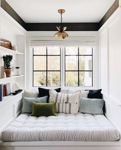 a white couch sitting under a window next to a shelf filled with lots of books