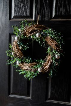 a wreath hanging on the front door of a house with greenery and ornaments around it