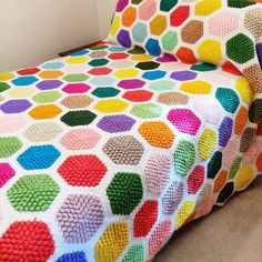 a multicolored crocheted blanket sitting on top of a bed next to a pillow