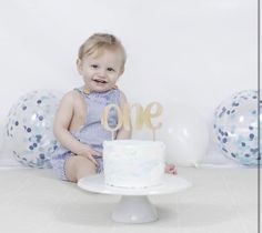 a baby sitting in front of a cake and balloons