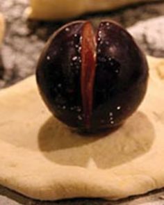 an uncooked plum sitting on top of a piece of dough with icing