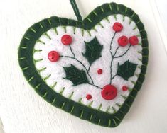 a felt ornament with holly leaves and red buttons in the shape of a heart