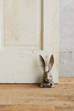 a small metal rabbit sitting on top of a wooden floor next to a white door