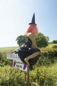 a scarecrow sitting on top of a sign in the middle of a grassy field