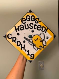 a hand holding up a yellow and white graduation cap