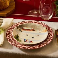 a plate with a christmas scene on it sitting on a table next to wine glasses