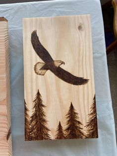 an eagle painted on wood with pine trees