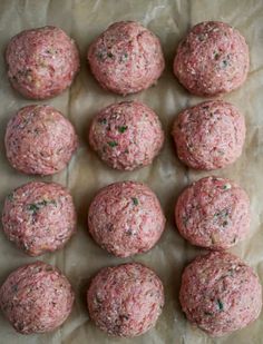 raw meatballs are lined up on a sheet of wax paper and ready to be cooked