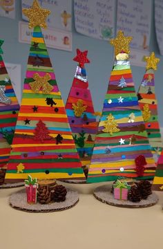 colorful christmas trees made out of paper and pine cones with presents on the table next to them