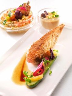 a white plate topped with fish and veggies next to a bowl of sauce