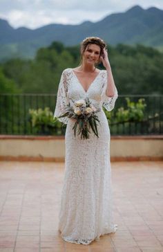 a woman in a white wedding dress standing on a brick floor with mountains in the background