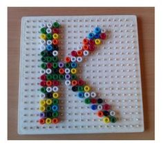 the letter k made out of legos is displayed on a white board with multicolored beads