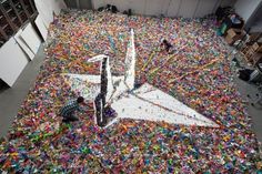 an airplane made out of plastic bottles in a room filled with other items and people