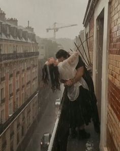 a man and woman kissing on top of a building in the rain with buildings behind them