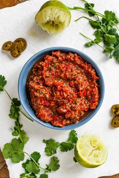 a blue bowl filled with salsa next to limes and cilantro