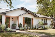 a white house with brown shutters and green plants in the front yard on a sunny day