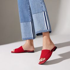 a woman's feet in red slippers and jeans, standing on a white surface