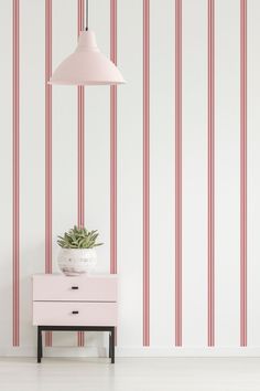 a pink dresser with a potted plant on it in front of striped wallpaper