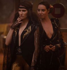 two women dressed in black and gold posing for the camera with their hands on their hips