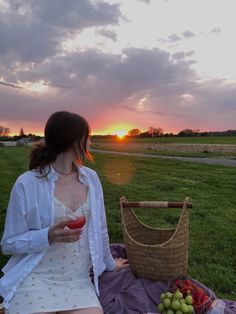 a woman sitting on a blanket holding a drink in her hand and looking at the sunset