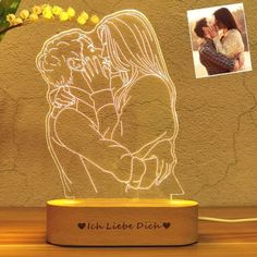 a couple kissing on their forehead with an illuminated photo next to it and a vase full of flowers