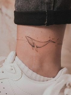 a woman's ankle with a small whale tattoo on her left side ribcage