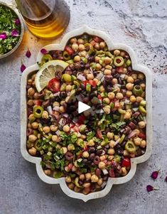 a platter filled with beans and vegetables next to a glass of olives on a table