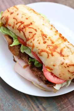 a sandwich with meat, tomatoes and lettuce on a white plate sitting on a wooden table