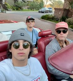 three men sitting in the back of a red convertible car with one man wearing sunglasses