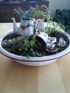 a white tea pot filled with plants on top of a wooden table