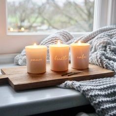 three lit candles sitting on top of a wooden tray next to a window sill