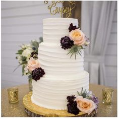 a white wedding cake with flowers on the top and gold trimmings is sitting on a table