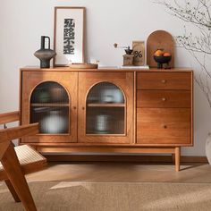 a wooden cabinet with glass doors in a living room next to a chair and vase