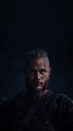 a man with a goatee and beard standing in front of a dark background, looking at the camera