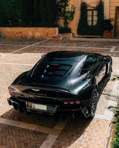 a black sports car parked in front of a building on a brick driveway with trees and bushes