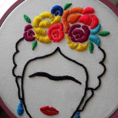 a woman's face with flowers in her hair is embroidered onto a white piece of fabric