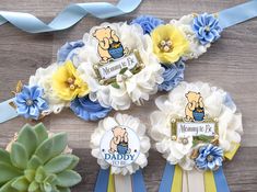 three baby shower decorations with flowers and ribbons on a wooden table next to a succulent plant