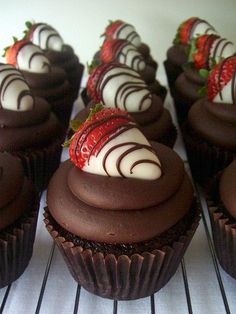 chocolate cupcakes with white frosting and strawberries on top are sitting on a wire rack