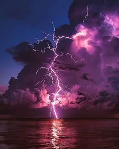 a lightning bolt is seen in the sky above water and clouds at night with purple hues