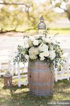 a wooden barrel with white flowers and greenery on the side for an outdoor ceremony